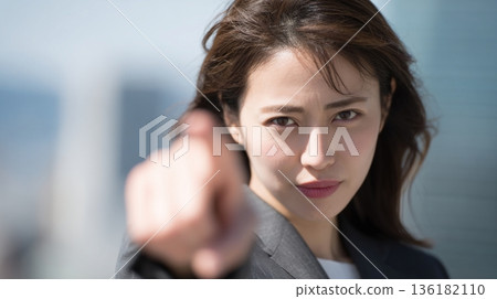A Japanese woman looks straight at the camera and points her finger 136182110