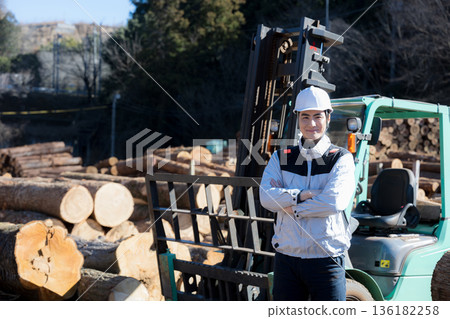 一名工人駕駛堆高機運送木材，雙手交叉抱在胸前，看向鏡頭。 136182258