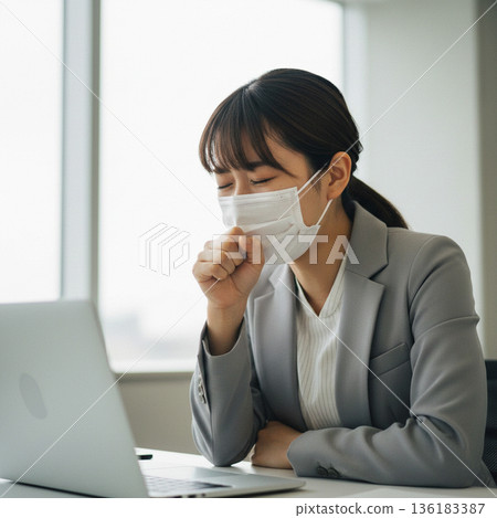 An unwell female office worker wearing a mask and coughing in the office. Image of a cold or infectious disease epidemic. An unwell female office worker wearing a mask and coughing in the office. Image of a cold or infectious disease epidemic. 136183387