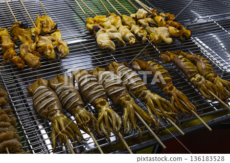 Marinated Squid Skewers On Grill Rack, A sizzling photo of marinated squid , glossy tentacles and charred edges glistening with marinade in grill, for seafood BBQ or street food documentary. Marinated Squid Skewers On Grill Rack, A sizzling photo of marinated squid , glossy tentacles and charred edges glistening with marinade in grill, for seafood BBQ or street food documentary. 136183528