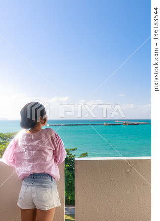 A woman's back view looking at the ocean in Okinawa. A peaceful time spent at the resort. 136183544