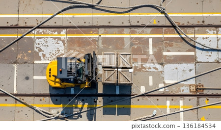 Aerial View Of Yellow Machinery Transporting Wooden Crate On Deck With Metal Chains And Lines Under Bright Sunlight 136184534