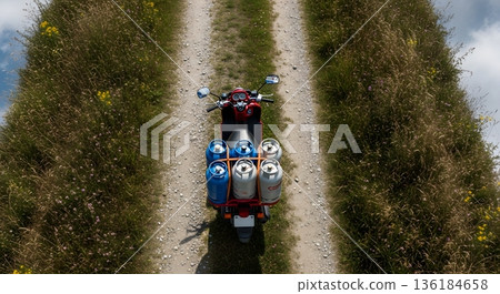 Motorcycle Transporting Propane Tanks on Dirt Road Surrounded by Wildflowers Under Clear Blue Sky 136184658