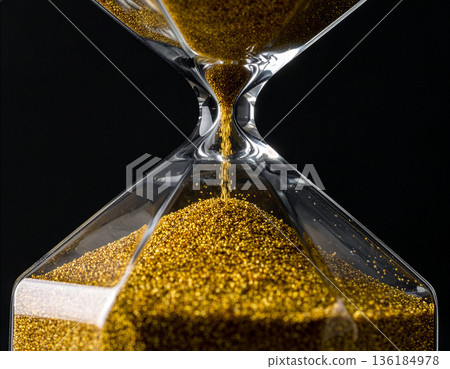 Close-up of a modern hourglass with flowing golden sand on a black background, time management concept 136184978