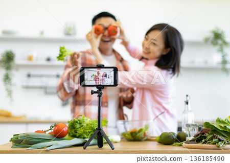 A happy couple films a cooking tutorial in their bright, modern kitchen, using fresh ingredients 136185490