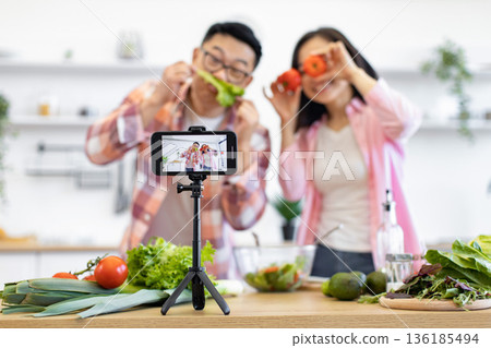 A cheerful couple is filming a cooking video in their kitchen, using fresh vegetables for fun 136185494