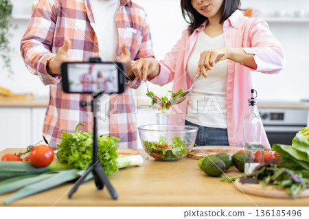 A couple is preparing a fresh salad in their kitchen while recording a video for their online audience A couple is preparing a fresh salad in their kitchen while recording a video for their online audience 136185496