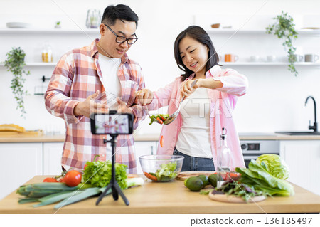 An Asian couple is preparing a salad while recording a cooking video for their online audience An Asian couple is preparing a salad while recording a cooking video for their online audience 136185497