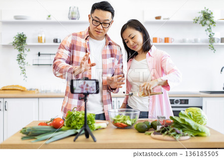 An Asian couple is preparing a salad in their kitchen while recording a video for their followers An Asian couple is preparing a salad in their kitchen while recording a video for their followers 136185505