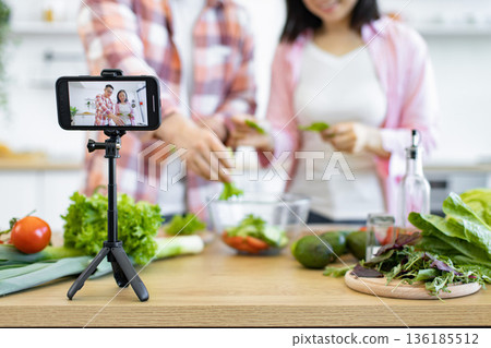 A couple is preparing a salad in their kitchen while recording a video for social media A couple is preparing a salad in their kitchen while recording a video for social media 136185512