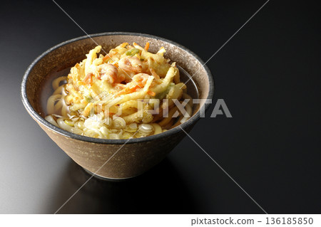 Shrimp and vegetable tempura udon noodles photographed against a black background 136185850