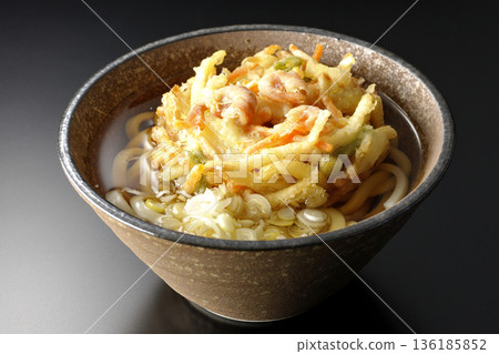 Shrimp and vegetable tempura udon noodles photographed against a black background 136185852