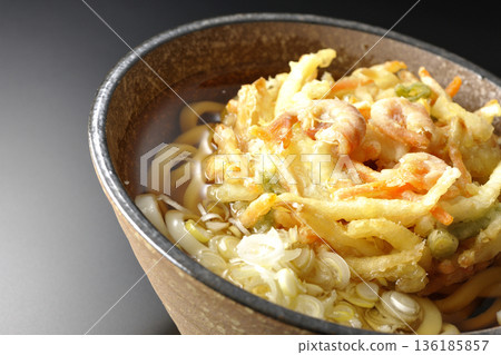 Shrimp and vegetable tempura udon noodles photographed against a black background 136185857
