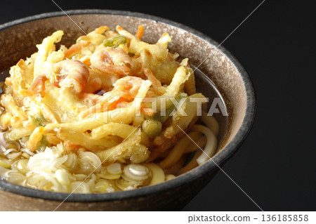 Shrimp and vegetable tempura udon noodles photographed against a black background 136185858
