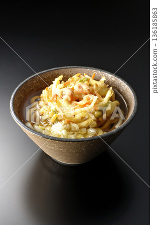 Shrimp and vegetable tempura udon noodles photographed against a black background 136185863