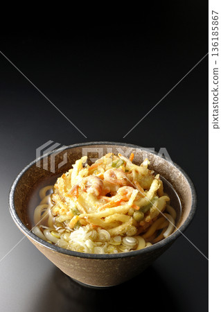 Shrimp and vegetable tempura udon noodles photographed against a black background 136185867