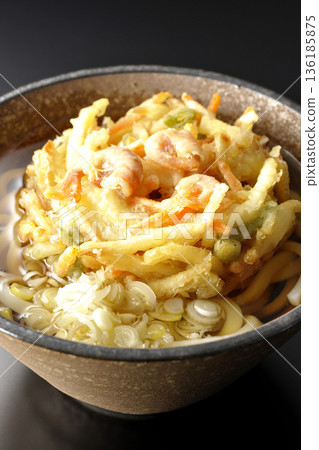 Shrimp and vegetable tempura udon noodles photographed against a black background 136185875