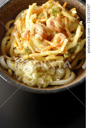 Shrimp and vegetable tempura udon noodles photographed against a black background 136185897