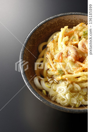 Shrimp and vegetable tempura udon noodles photographed against a black background 136185899