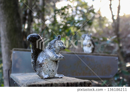 Two well-worn statues of squirrels placed on a wooden sign in the park Two well-worn statues of squirrels placed on a wooden sign in the park 136186211