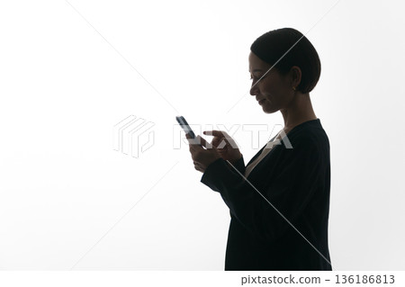 一位女性側臉的剪影,她正看著一部智慧型手機 一位女性側臉的剪影,她正看著一部智慧型手機 136186813