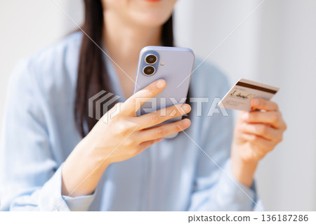 一名女子一邊操作智慧型手機一邊查看信用卡 一名女子一邊操作智慧型手機一邊查看信用卡 136187286