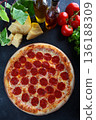 Classic pizza with spicy pepperoni sausage. A popular filling. Pieces of hard cheese are laid out on the table. Top view. 136188309