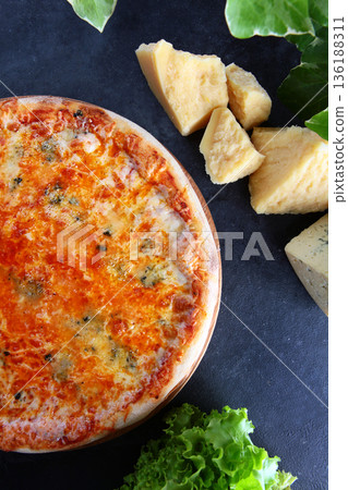 Classic Italian pizza with four types of cheese. There are slices of cheese and lettuce leaves on the table next to it. Top view. Black background. 136188311