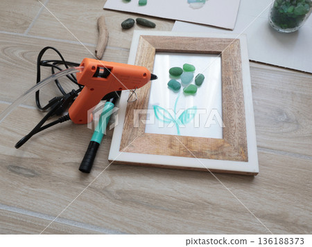 Sea glass flower in frame. Making art from natural materials. Glue gun and driftwood for picture. Hobbies and creativity. Reuse and nature, ecology.  136188373