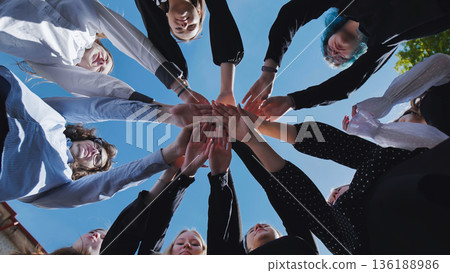 Students joining hands in a circle, celebrating their school day achievement beneath a clear blue sky Students joining hands in a circle, celebrating their school day achievement beneath a clear blue sky 136188986