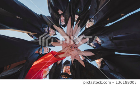 Students in graduation gowns come together in a circle to celebrate their academic success Students in graduation gowns come together in a circle to celebrate their academic success 136189005