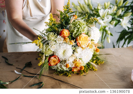 Artisan at work assembles floral bouquet with roses and hydrangeas during flower workshop. Handmade floral arrangement, flower workshop, artisan at work. 136190078