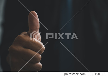 Sign of approval shows a man hand pose with a thumbs up gesture in a closeup, this positive sign communicates success and agreement against a dark professional background Sign of approval shows a man hand pose with a thumbs up gesture in a closeup, this positive sign communicates success and agreement against a dark professional background 136190118