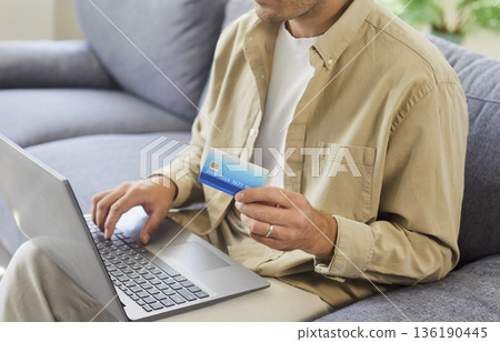 Man with laptop and credit card at home, verifying online payment details 136190445
