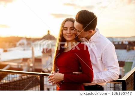 Couple stands on a rooftop during sunset while sharing a loving moment in the city 136190747