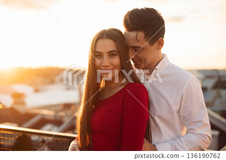 Couple enjoys sunset on rooftop while sharing a moment together in a city during warm evening hours 136190762