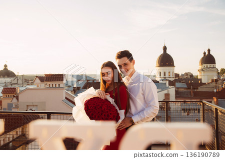 Couple celebrates special moment with roses on rooftop during sunset in city 136190789