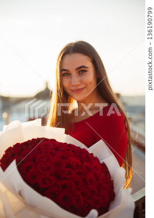Woman holds large bouquet of red roses during sunset at outdoor location in city 136190799