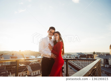 Couple stands together on a rooftop with city view during sunset in a relaxed moment Couple stands together on a rooftop with city view during sunset in a relaxed moment 136190815