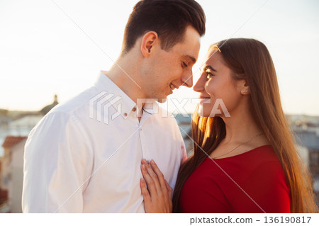 Couple enjoying a sunset together while standing close in a city setting Couple enjoying a sunset together while standing close in a city setting 136190817