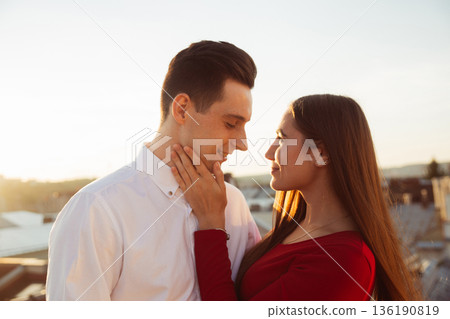 Couple shares a moment together during sunset on a rooftop in a city setting while enjoying each others company Couple shares a moment together during sunset on a rooftop in a city setting while enjoying each others company 136190819