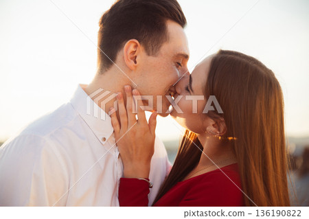 Couple kisses during sunset on a rooftop while enjoying a moment together in the warm evening light 136190822