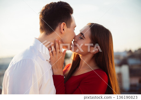 Couple shares a kiss on a rooftop during sunset in a city setting with buildings in the background Couple shares a kiss on a rooftop during sunset in a city setting with buildings in the background 136190823