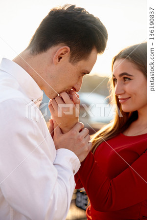 Couple sharing a moment together near water during sunset while engaged in a tender gesture of affection Couple sharing a moment together near water during sunset while engaged in a tender gesture of affection 136190837