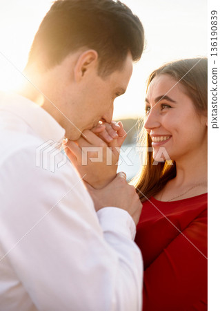Couple shares a moment together at sunset by the water in a romantic setting with smiles and gestures 136190839