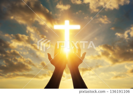 Human hands open palm up worshiping a glowing Christian cross in sunset sky. Concept for faith, spirituality, and hope. Human hands open palm up worshiping a glowing Christian cross in sunset sky. Concept for faith, spirituality, and hope. 136191106