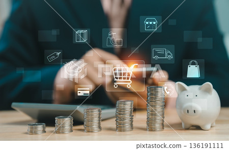 Businessman using smartphone with shopping cart icon, piggy bank and coins stack. Concept of online shopping, e-commerce, and financial saving plan. Businessman using smartphone with shopping cart icon, piggy bank and coins stack. Concept of online shopping, e-commerce, and financial saving plan. 136191111