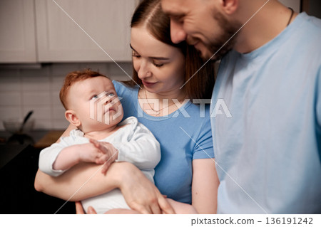 Loving family moment with parents and baby in cozy kitchen setting showcasing warmth, connection, and joy of parenthood, family bonding concept 136191242