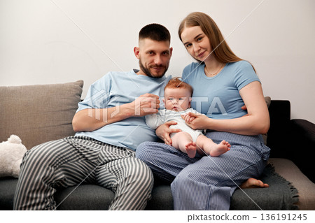 Family portrait with parents holding baby on couch in cozy living room showcasing love and connection in a nurturing environment family bonding concept 136191245