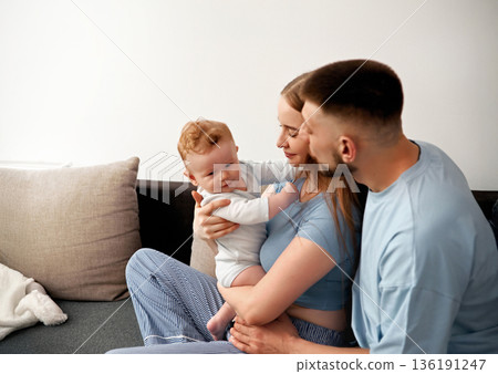 Loving family moment with parents and baby on couch in cozy living room showcasing warmth, connection, and joy in family life, family bonding concept Loving family moment with parents and baby on couch in cozy living room showcasing warmth, connection, and joy in family life, family bonding concept 136191247